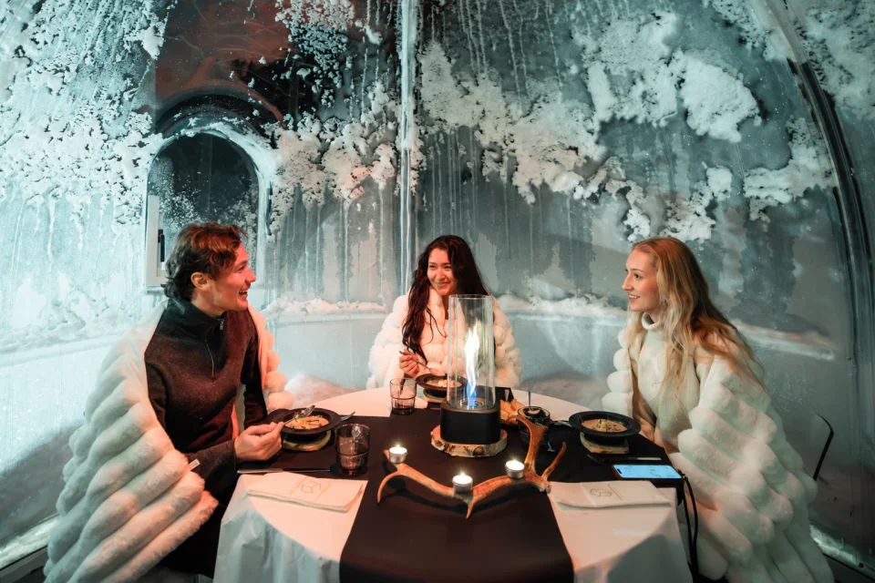 Three guests sharing dinner and laughter inside an Aurora Dinner Dome