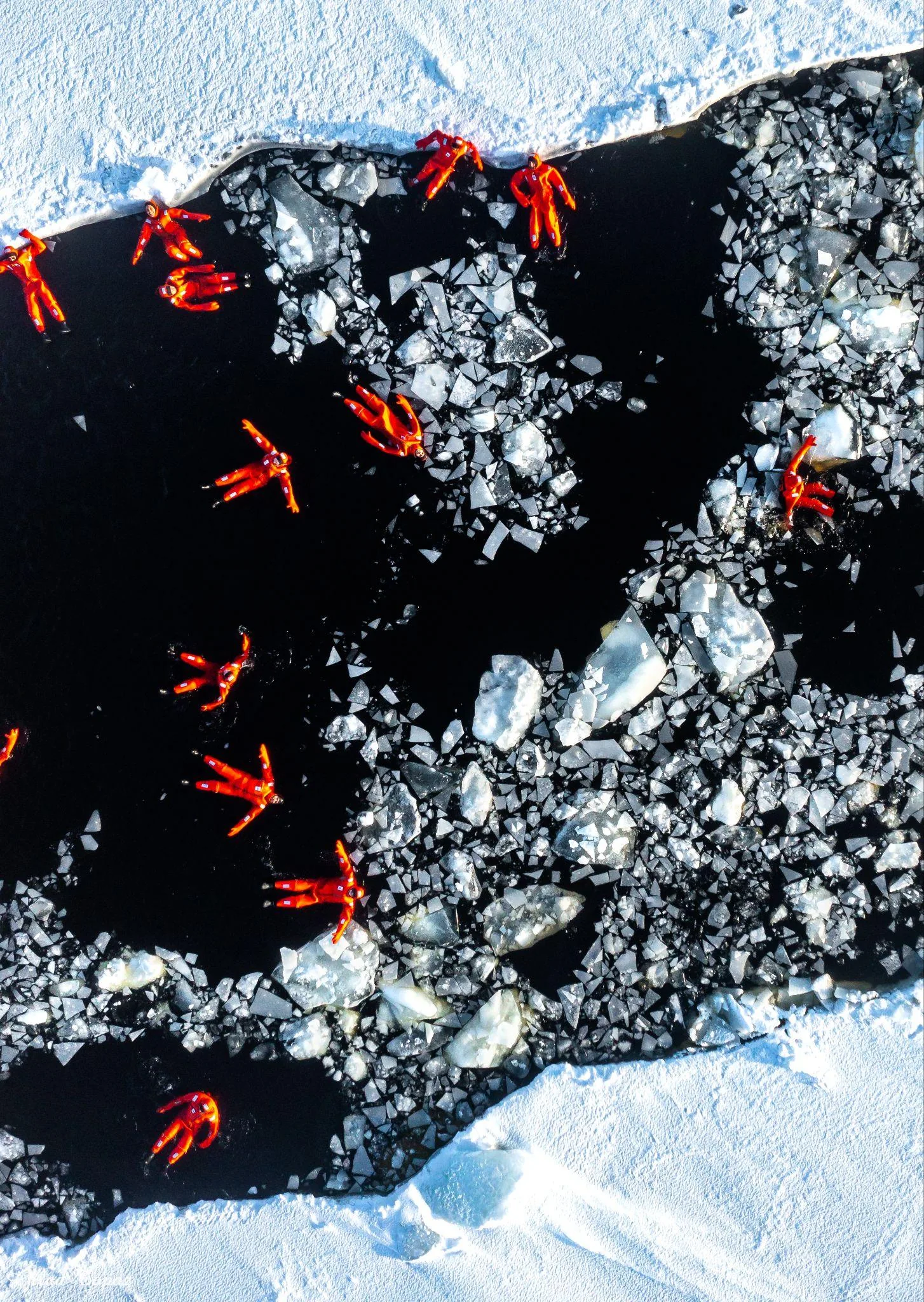 Des personnes en combinaisons de survie orange flottent parmi les glaces de mer