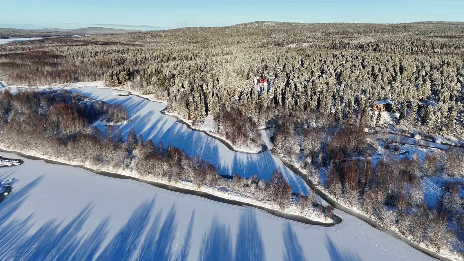 Verschneiter Wald und Fluss Ounasjoki nahe der Lodge aus der Vogelperspektive