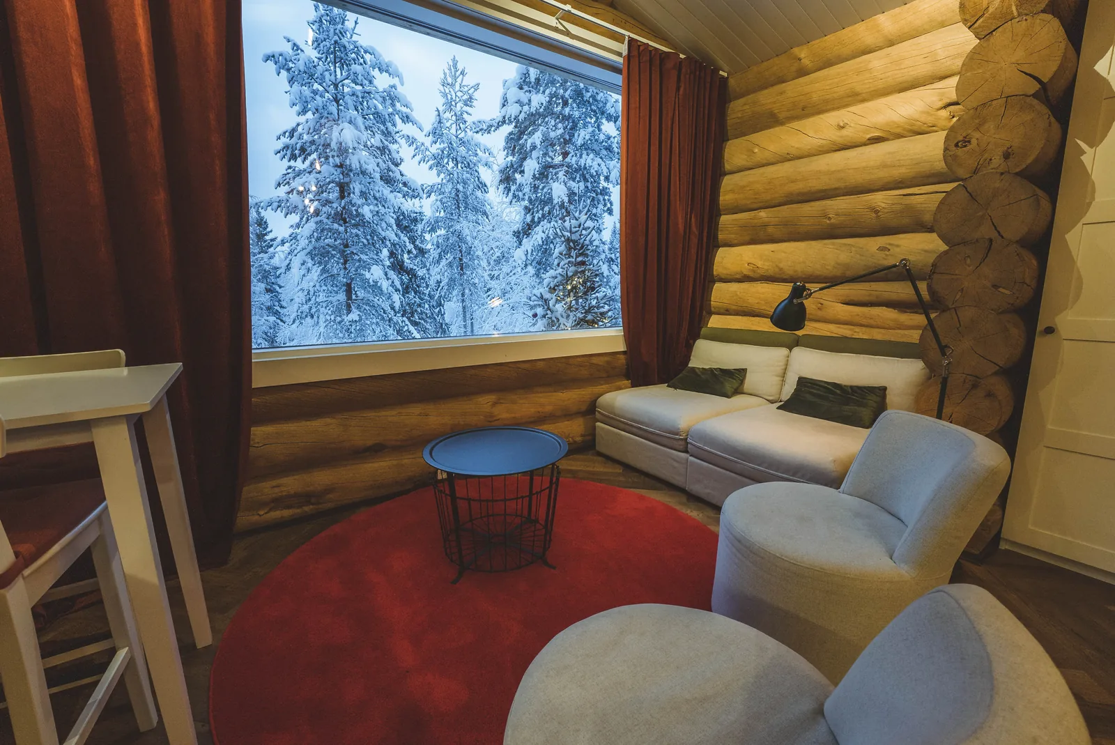 Wohnbereich der gemütlichen Blockhütte mit Blick auf den verschneiten Wald