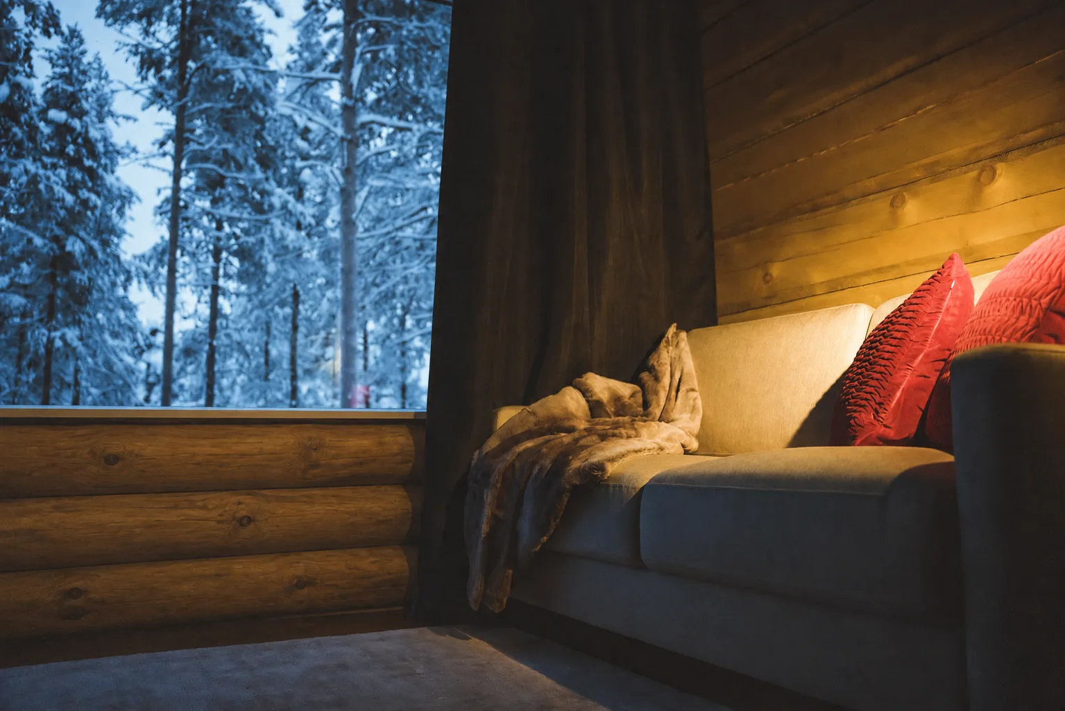 Sofa der gemütlichen Blockhütte neben einem Fenster zum verschneiten Wald