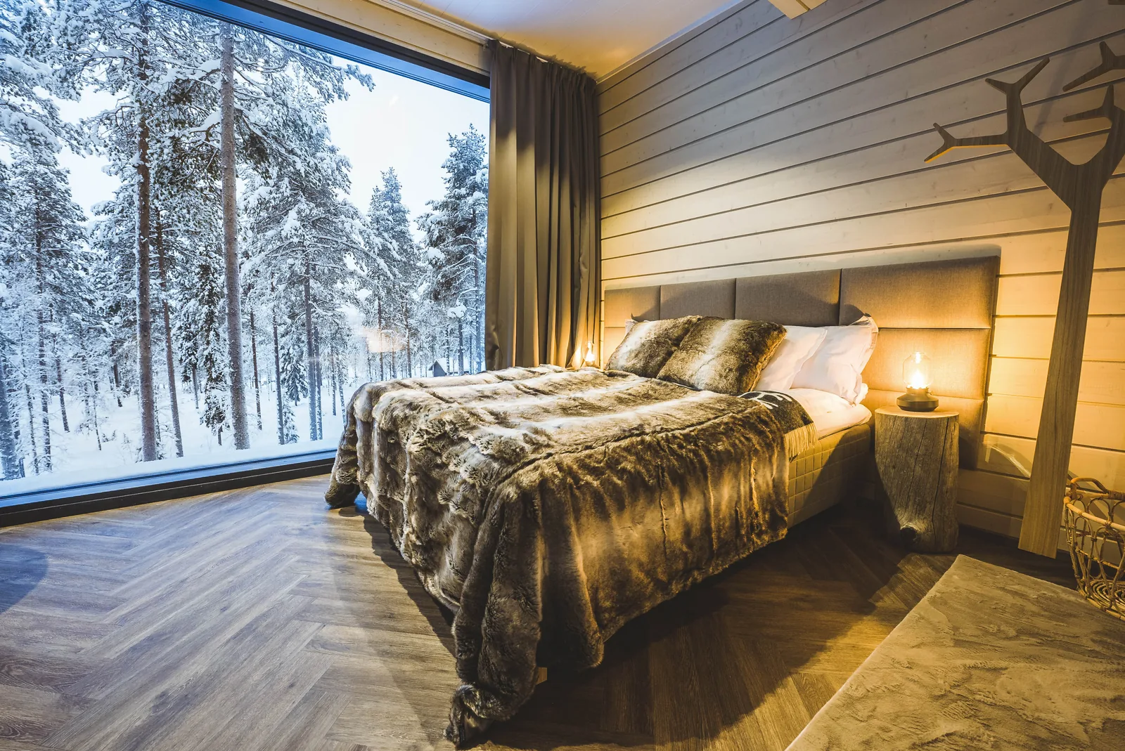 Bett der Invisible Suite vor einem Panoramafenster zum verschneiten Wald