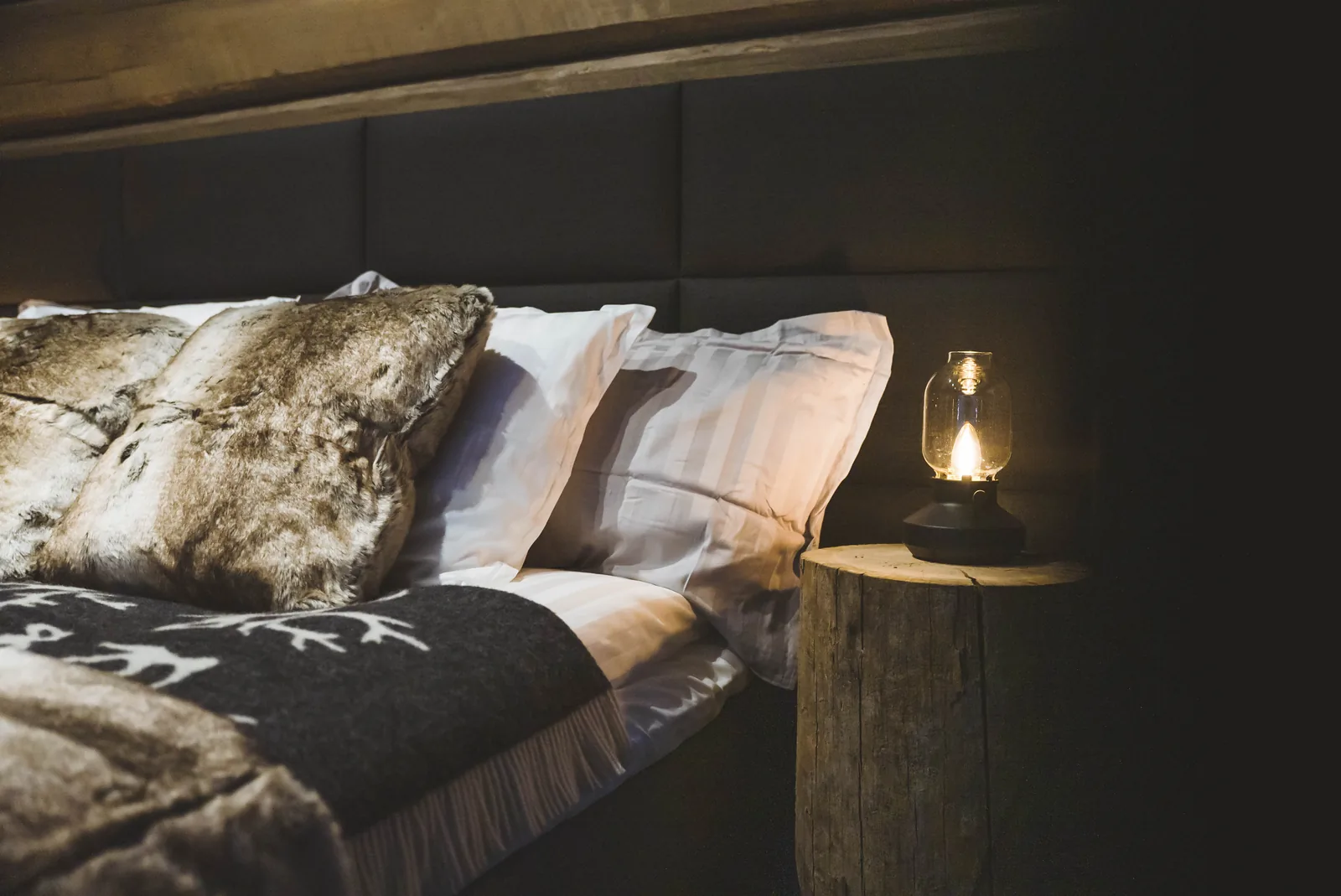 Detail des Bettes einer Invisible Suite mit Felldecken und Laterne