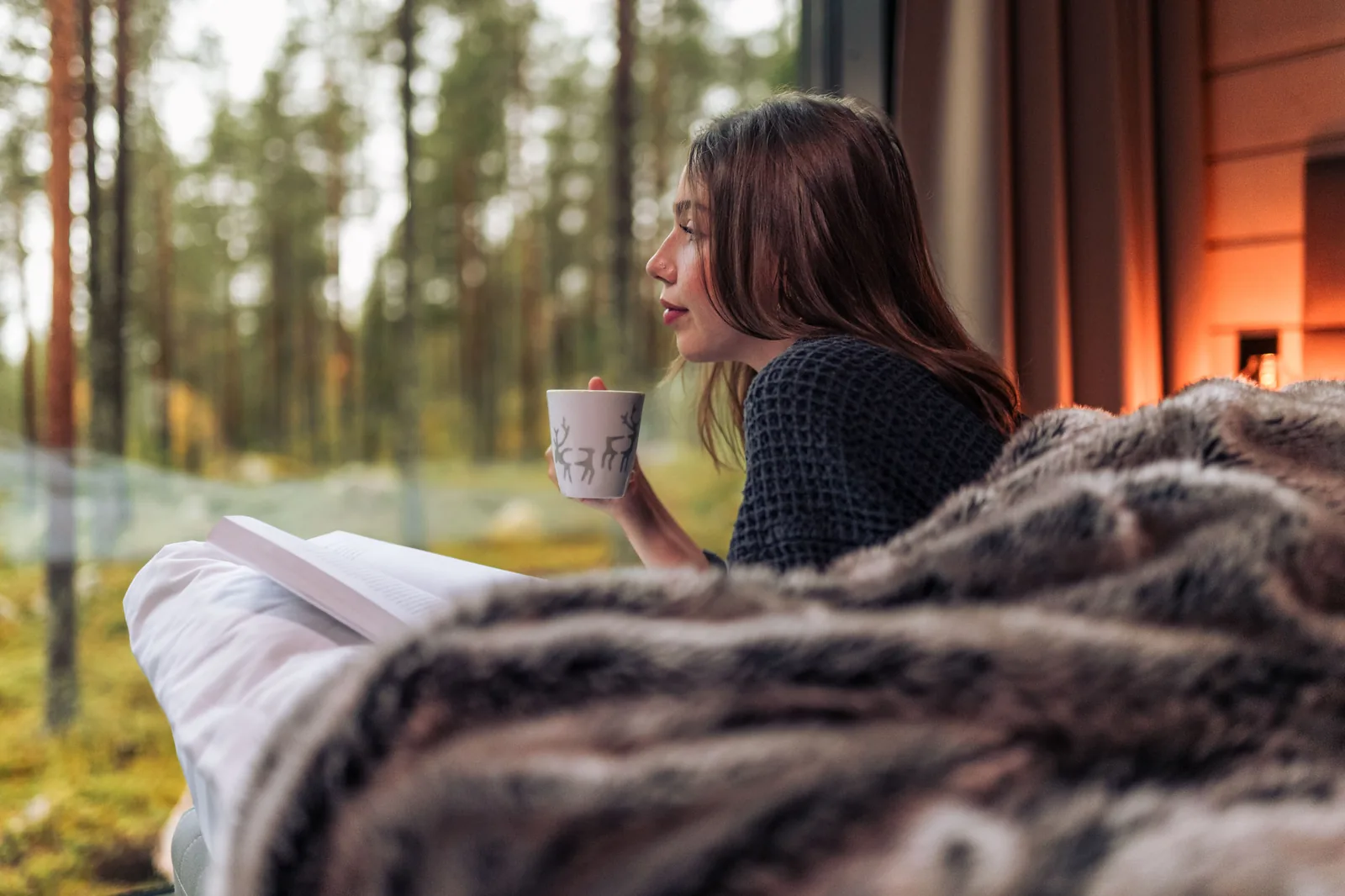 Gast mit Getränk am raumhohen Fenster zum Wald