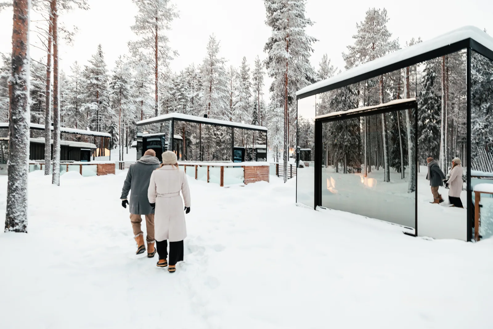 Gäste spazieren zwischen verspiegelten Invisible Suites im verschneiten Wald